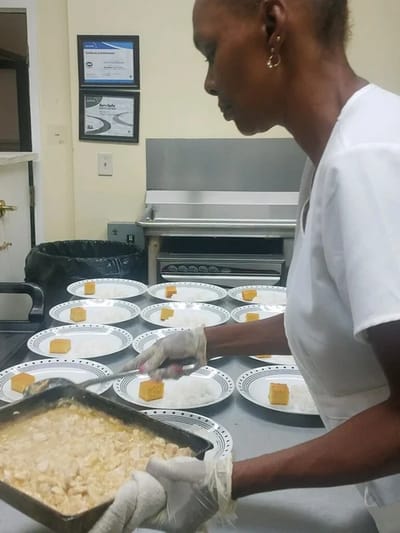 Staff member serving meals in the dining area.