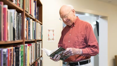 Elderly man reading a book in a library.