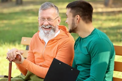 Two men laughing on a park bench outdoors.