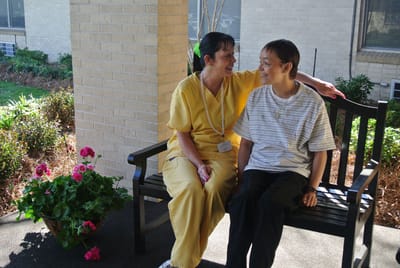 Staff member and resident smiling on a bench outside.