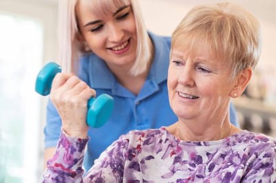 A staff member assisting a resident with weights in a bright room
