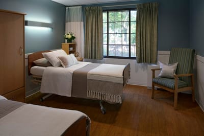 Brightly lit resident room with two beds and a chair