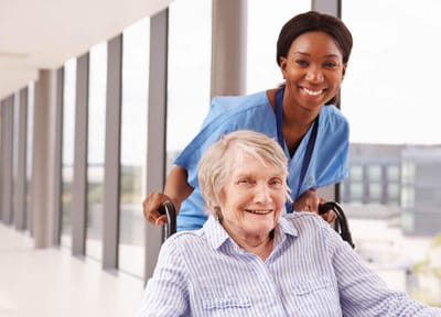 Resident in a wheelchair with a caregiver in a bright hallway