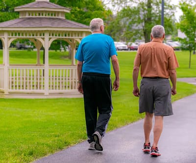 Two residents walking in a garden area near a gazebo