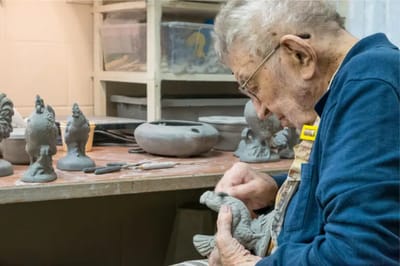An elderly man carving a sculpture in an activity room