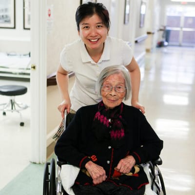 A caregiver smiling behind an elderly resident in a hallway