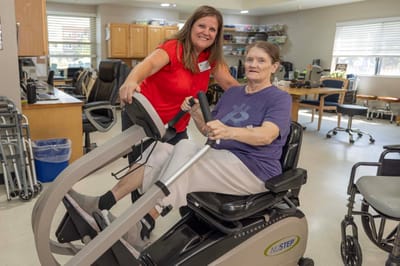 Staff member assisting a resident with exercise equipment.