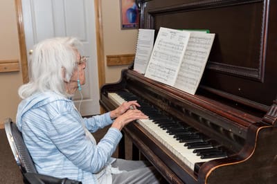 An elderly woman playing piano in a communal area