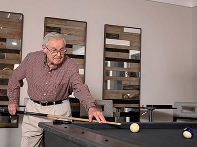 An elderly man playing pool in a recreational room