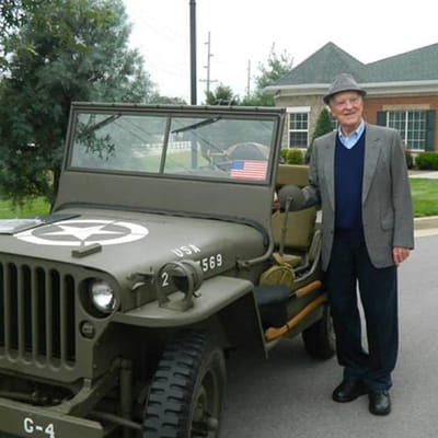 An elderly man beside a vintage military jeep outside the facility