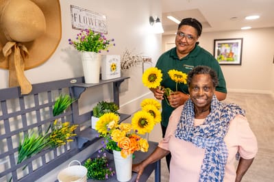 Resident and staff member arranging flowers in a bright interior space