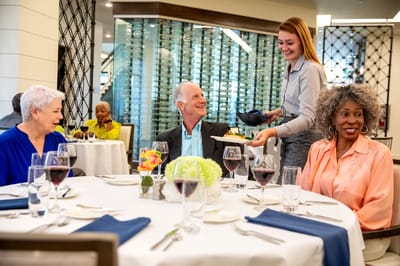 Residents enjoying a meal served by staff in a dining area