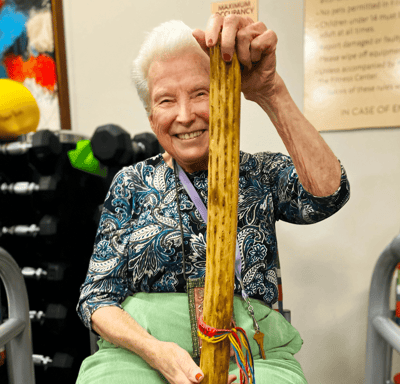 Resident smiling and holding a large stick in an activity room