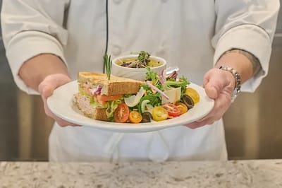 A chef presenting a plate with sandwich and salad