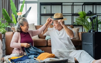 Two seniors playfully packing a suitcase in a living area