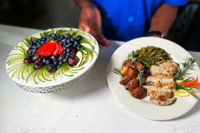 A chef presenting a gourmet meal with vegetables and dessert