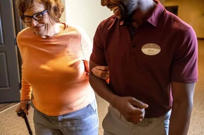 A senior resident walking with a staff member in a corridor