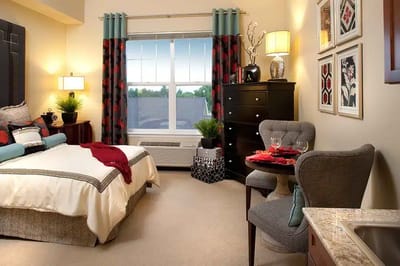 A cozy, furnished resident room with a window view