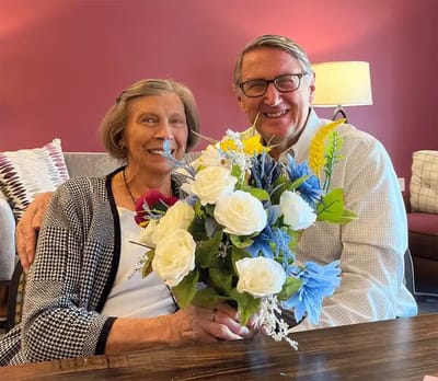 A resident and family member posing with a flower bouquet