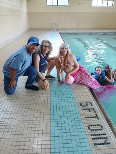 Residents and staff interacting with a mermaid by the pool