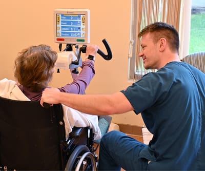 Therapist assisting resident with exercise equipment.