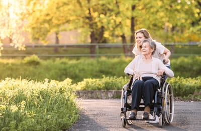 A caregiver assisting a senior woman in a wheelchair outdoors.