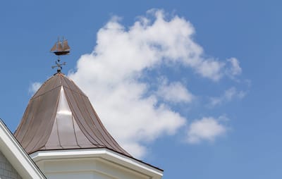 Weather vane atop a building under blue sky.