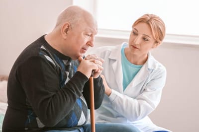 Caregiver assisting an elderly man with a cane.