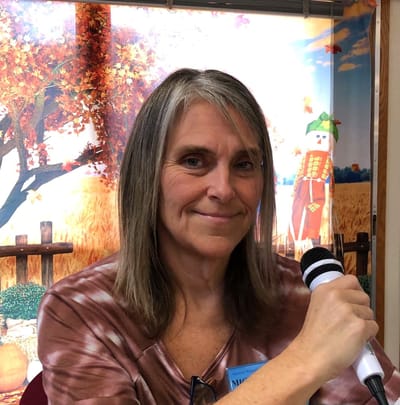 Woman speaking with a microphone in a decorated indoor setting.