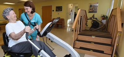 Staff assisting a resident with exercise equipment.