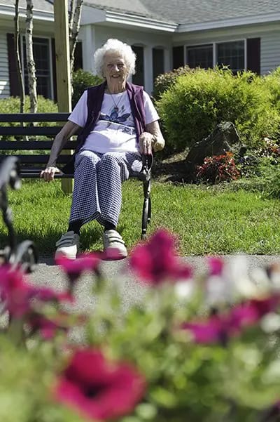 Elderly woman sitting on a bench in a garden.