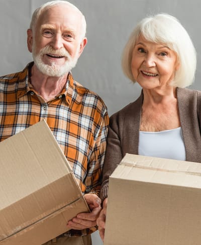 Two smiling seniors holding boxes together.