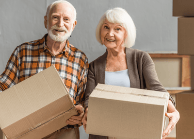 An elderly couple smiling while holding boxes.
