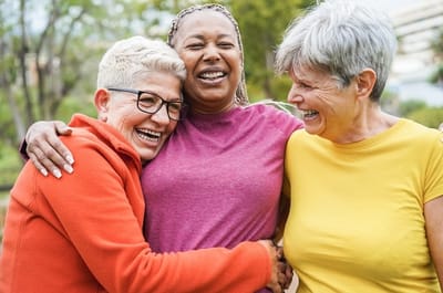 Three joyful women laughing together outdoors.