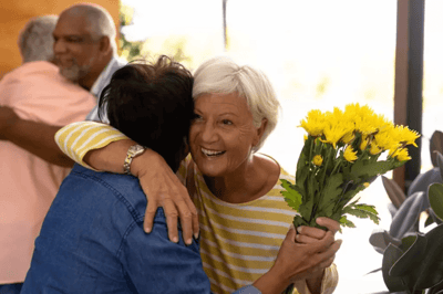 Residents embracing and celebrating with flowers indoors.