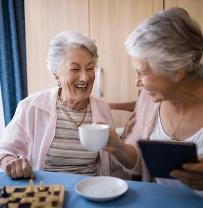 Two elderly women laughing and enjoying tea together.