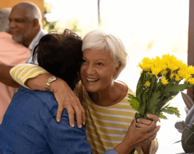 A joyful resident hugging a visitor with flowers.