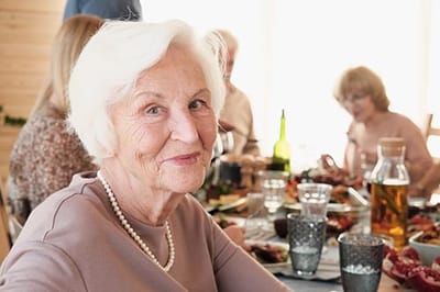 Smiling senior woman at a dining table with food.