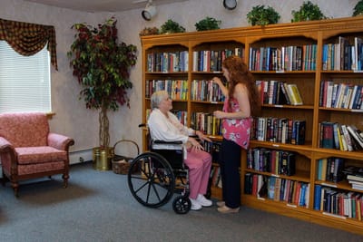 Resident in wheelchair with staff in library area.
