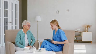 A nurse discussing with a senior resident indoors.
