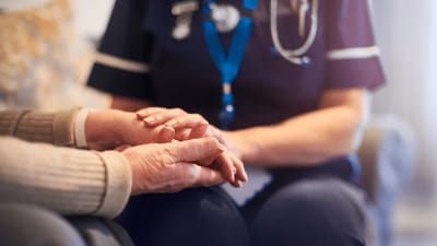 A caregiver holding an elderly person's hand