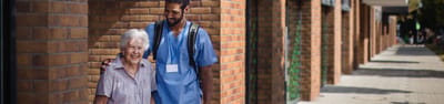 A caregiver and a senior walking outside.