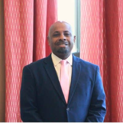 Man in a suit smiling indoors by curtains