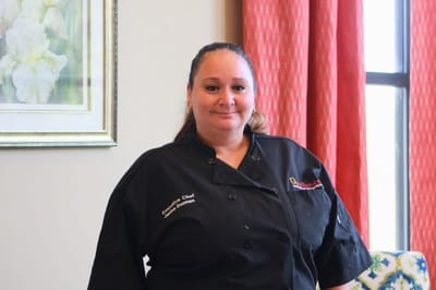 Chef in a uniform smiling in a dining area.