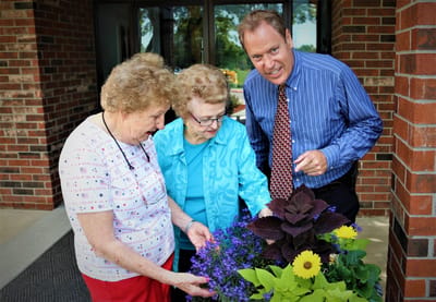 Harmony Court, independent living in Bakersfield, CA — Seniors and staff examining colorful flowers in planters