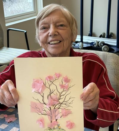 Resident holding up an art project with pink flowers