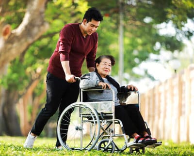 A caregiver assisting a senior woman in a wheelchair outdoors
