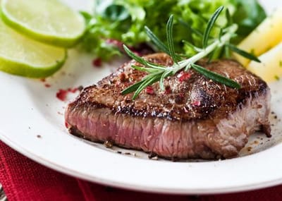 A plated steak with greens and lime slices
