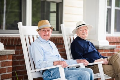 Two elderly men sitting on rocking chairs outside