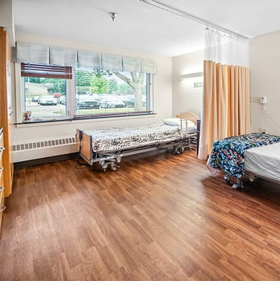 Good Samaritan Society Sioux Falls Village, Nursing Home in Sioux Falls, SD — Empty shared room with two hospital beds and wood flooring